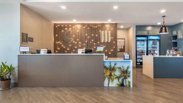 A reception area with a modern design, featuring a wooden panel wall with integrated lighting, a reception desk, and a refrigerator stocked with beverages. - Comfort Suites Fort Myers East I-75 (Fort Myers)