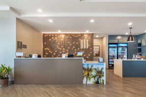 A reception area with a modern design, featuring a wooden panel wall with integrated lighting, a reception desk, and a refrigerator stocked with beverages. - Comfort Suites Fort Myers East I-75 (Fort Myers)