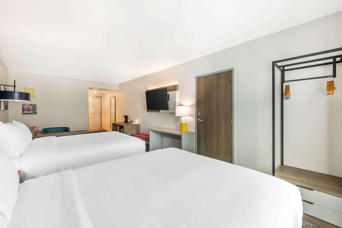 A hotel room with two beds, a desk, a TV, a wardrobe, and a mirror.