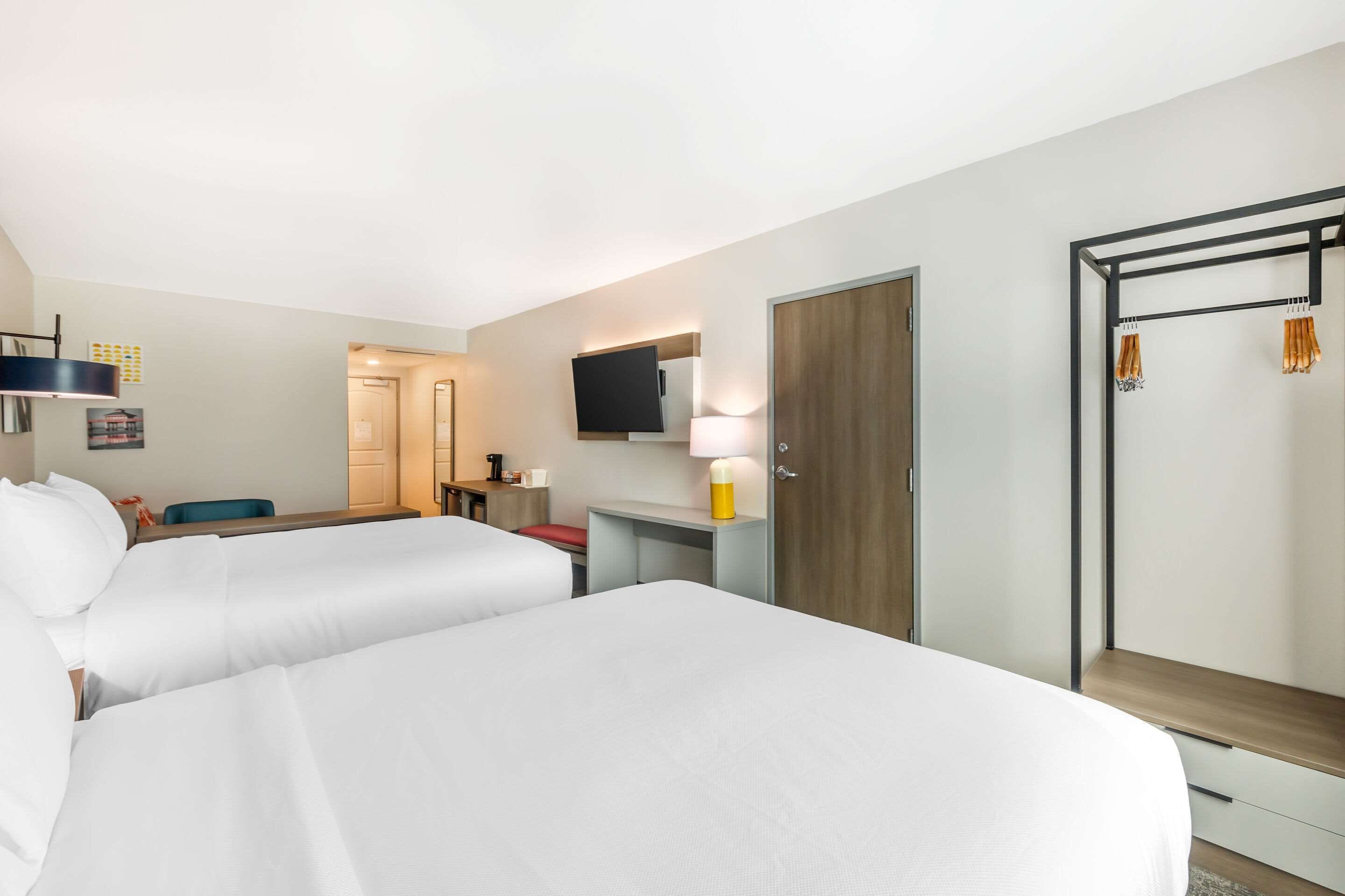 Une chambre d’hôtel avec deux lits, un bureau, une télévision, une armoire et un espace douche.