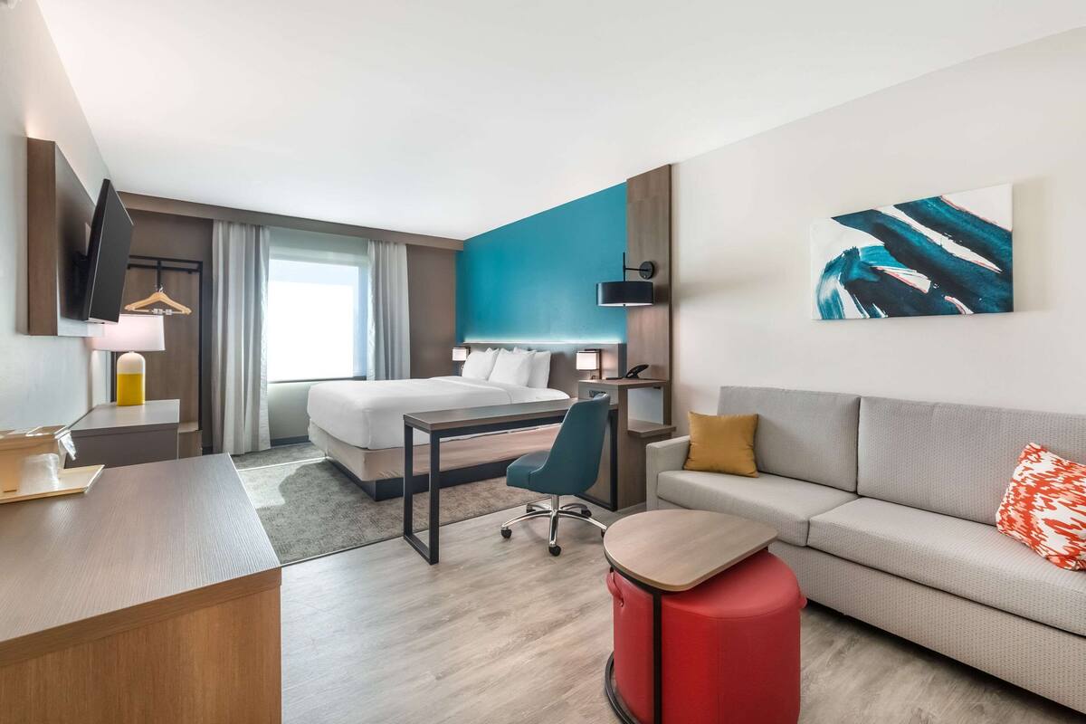 A modern hotel room with a bed, desk, chair, and sofa.