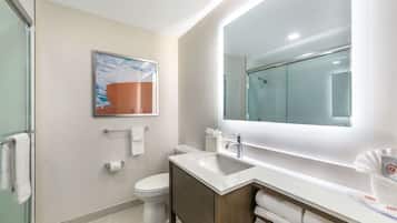 Un baño moderno con cabina de ducha de vidrio, un lavamanos blanco con espejo y un inodoro con toallero.