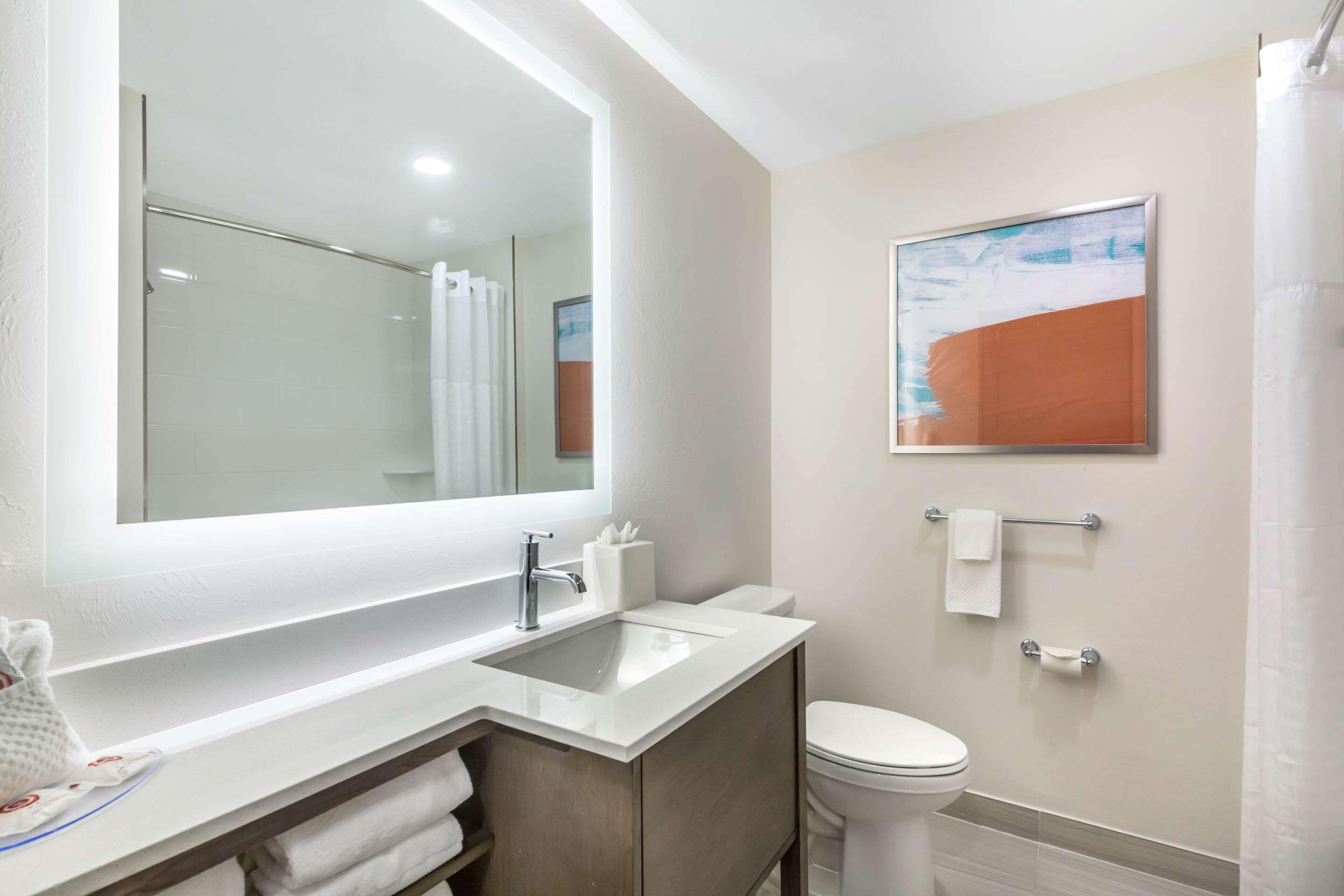A modern bathroom with a large mirror, a sink, a toilet, and a shower curtain.