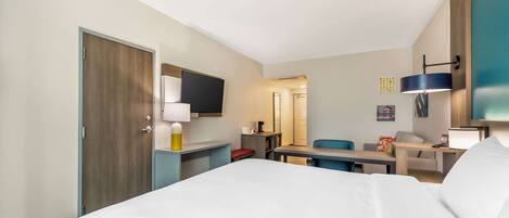 A hotel room with a bed, desk, chair, and a TV mounted on the wall.