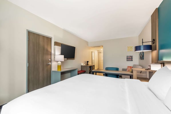 A hotel room with a bed, desk, chair, and a TV mounted on the wall.