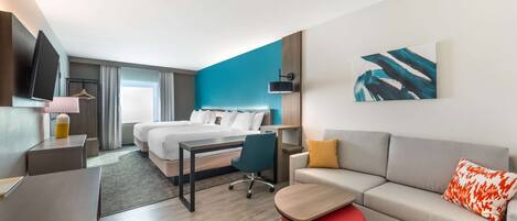 Una habitación de hotel moderna con una cama, un escritorio, un sofá y un reposapiés rojo.
