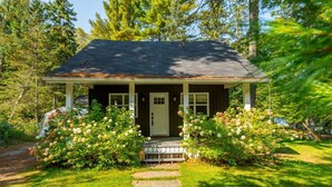 A small, single-story house with a porch, surrounded by lush greenery and flowering bushes. - Pet Friendly Fall Getaway  Waterfront (Huntsville)