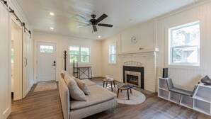 A spacious living room with a beige sofa, a fireplace, a ceiling fan, and large windows. - Pet Friendly Fall Getaway  Waterfront (Huntsville)