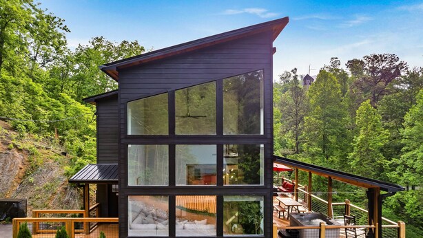 A modern cabin with large windows, a deck, and a view of the surrounding forest.