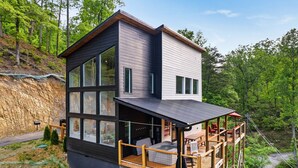 A modern two-story cabin with large windows, a deck, and a hot tub.