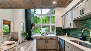 A modern kitchen with a large window, wooden flooring, and a green backsplash.
