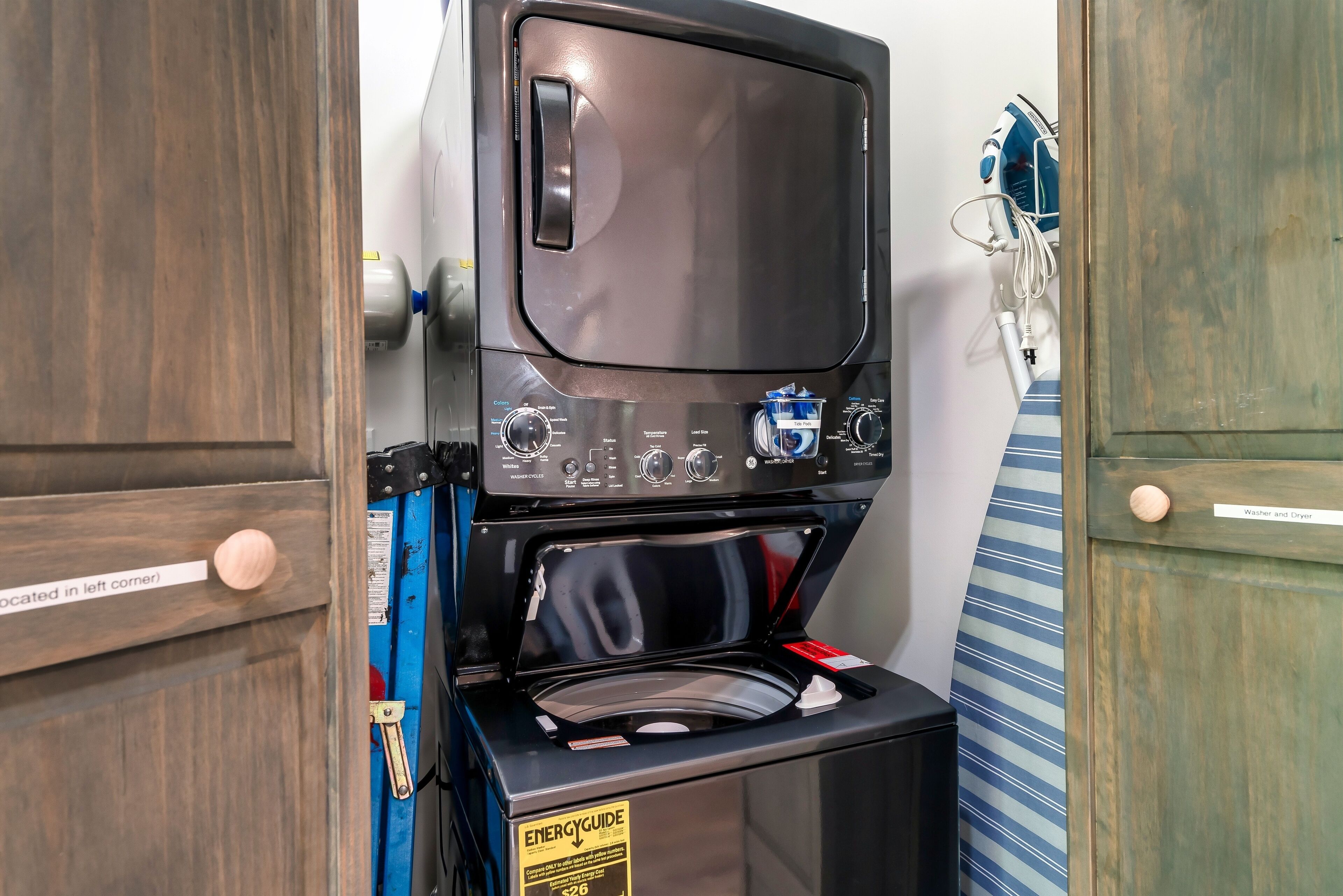 Un appareil compact combinant lave-linge et sèche-linge, doté d’un panneau de commande, installé dans un coin d’une pièce avec des portes en bois et un mur à rayures.