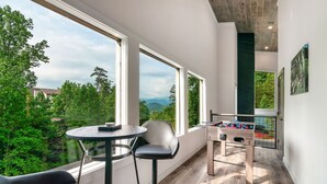 A modern room with large windows, a foosball table, and a round table with two chairs.
