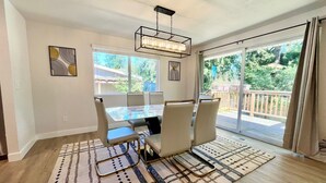 A dining area with a glass table and chairs, a patterned rug, and a view of a wooden deck and greenery. - Airy Modern Farmhouse 5BR/3BA Oasis w/ Fast Wi-Fi (Kent)