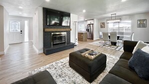 A modern living room with a fireplace, a dining area, and a kitchen. - Airy Modern Farmhouse 5BR/3BA Oasis w/ Fast Wi-Fi (Kent)