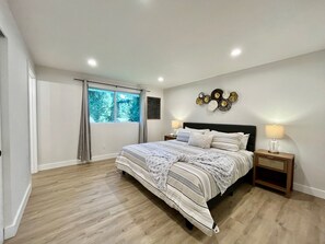 A bedroom with a bed, two bedside tables, a window with curtains, and a wall decoration.