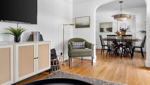 A modern living room with a dining area, featuring a rattan cabinet, a green armchair, a dining table with chairs, and a hanging light fixture. - Park Circle - Firefly - Renovated 3 Bedroom! (North Charleston)