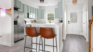 Una cucina moderna con mobili color verde chiaro, un frigorifero in acciaio inossidabile e due sgabelli da bar marroni.