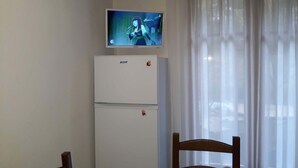A room with a white refrigerator, a television mounted above it, and a wooden chair. - 2* apartment in the mountains (Luz-Saint-Sauveur)