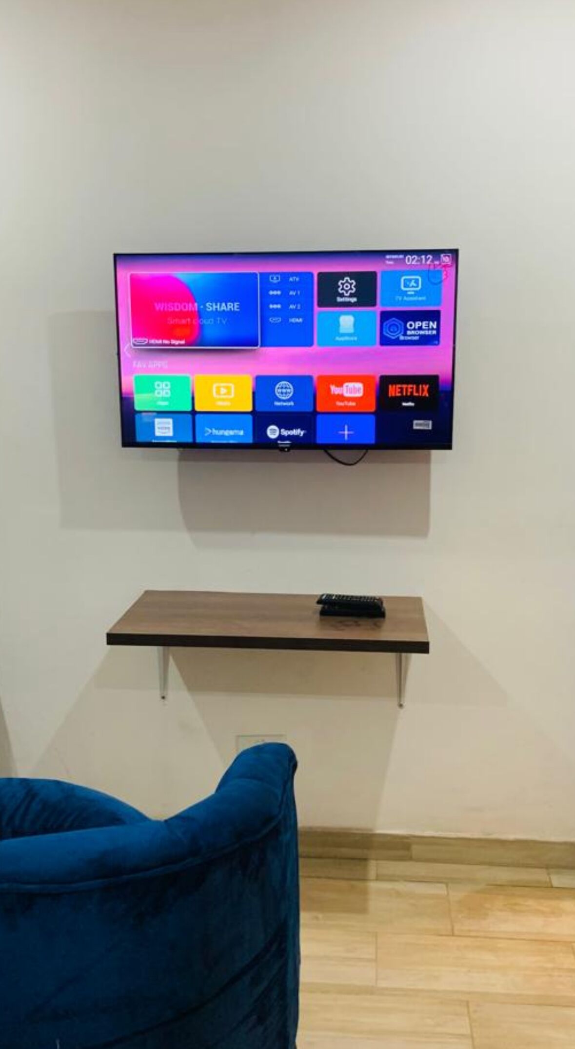 A flat-screen TV mounted on a wall with a remote control on a small shelf below it.