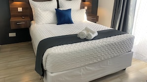 A neatly made bed with a white quilt, two pillows, and a folded towel on a dark-colored bedspread. - Mongi Guest House (Harare)