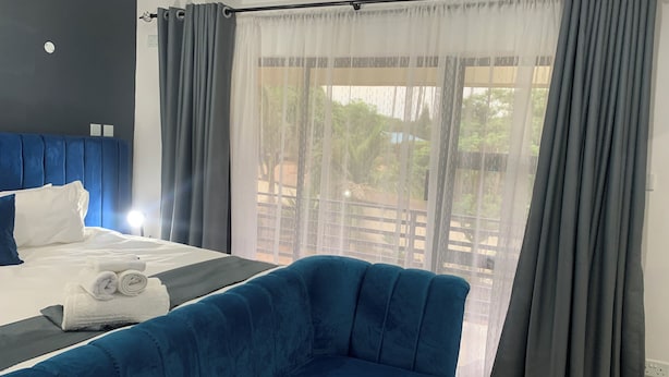A hotel room with a bed, a blue sofa, and a large window with curtains. - Mongi Guest House (Harare)