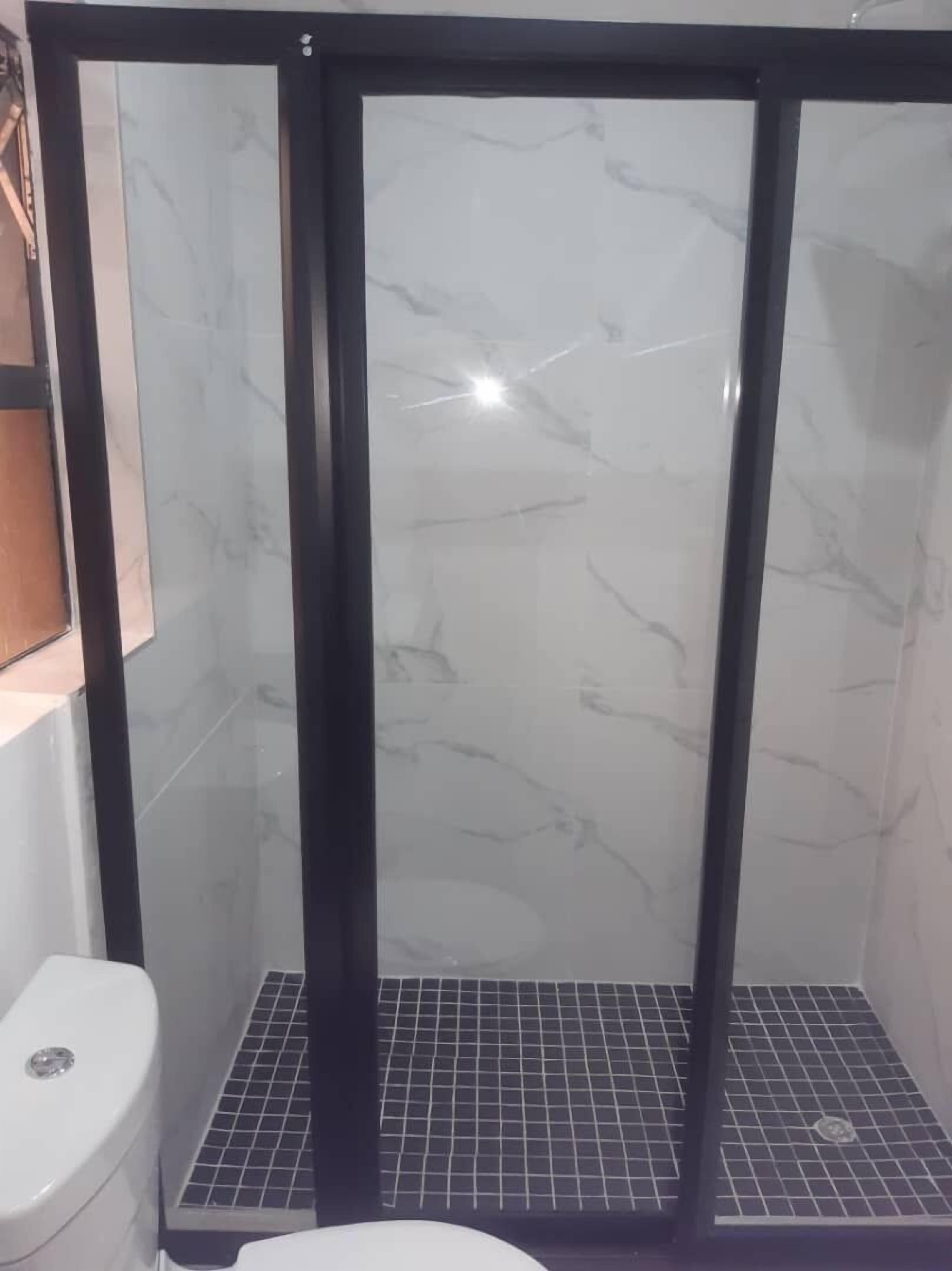 Une salle de bain avec une douche à parois de verre, des toilettes et un sol carrelé.