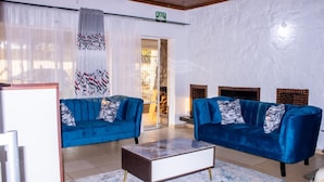 A modern living room with two blue sofas, a marble coffee table, and a fireplace. - Mongi Guest House (Harare)
