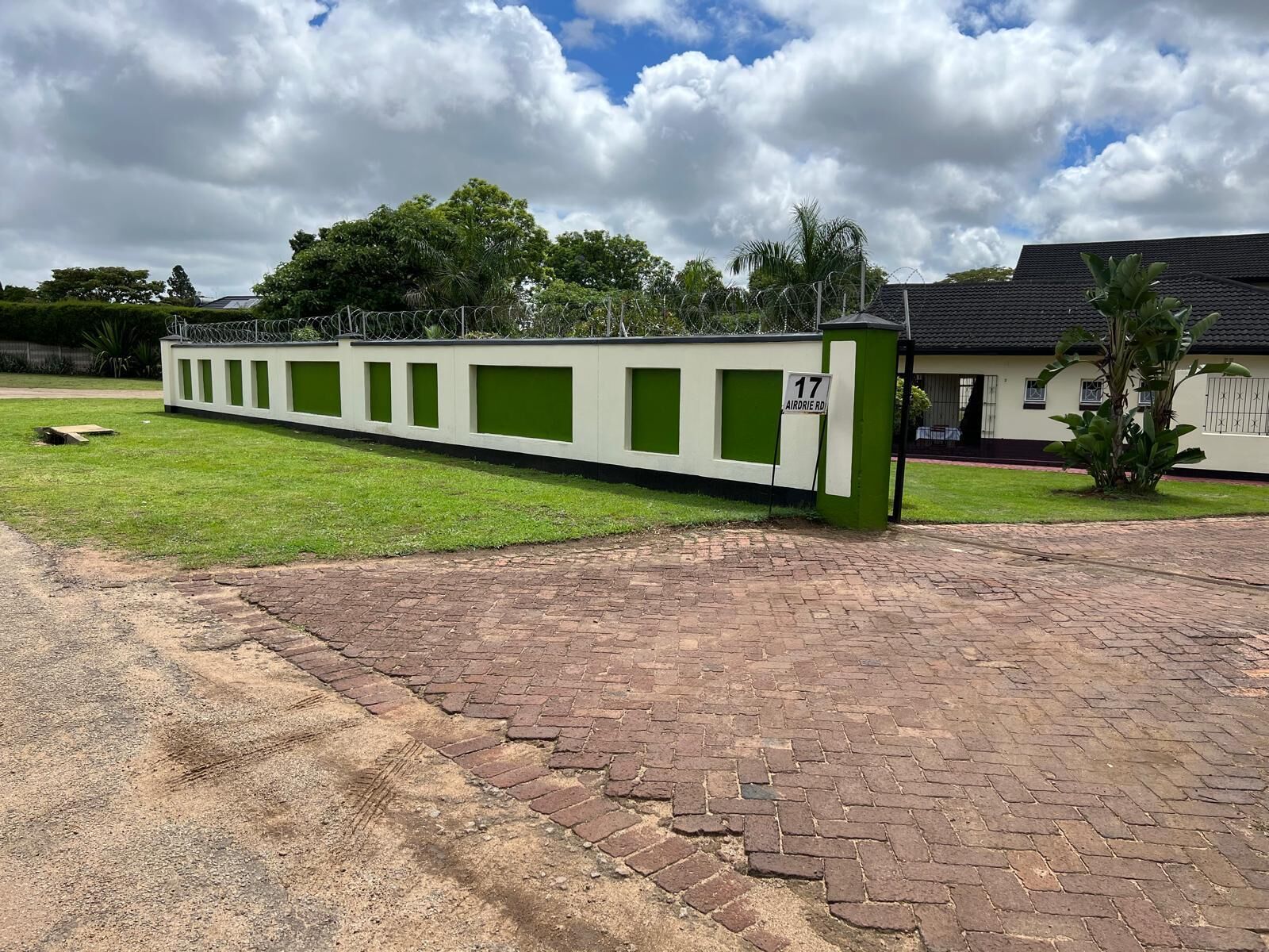 A long, narrow building with green and white panels, a brick pathway, and a sign indicating '17 Airdie Rd'.