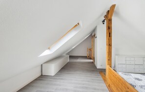 A room with a sloped ceiling, a wooden bench, a white cabinet, and a patterned bedspread.