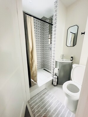 Ein Badezimmer mit Dusche, Toilette, Waschbecken und Spiegel.