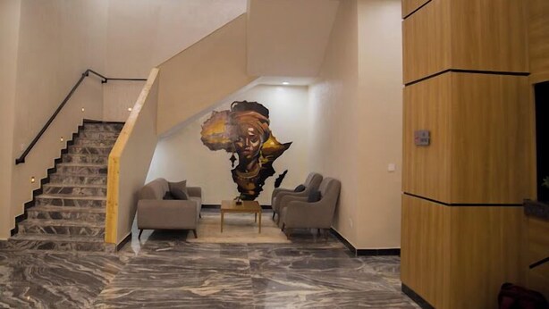 A modern lobby with a marble floor, a staircase, two sofas, and a large abstract artwork. - The Edge Hotel and Suites (Abuja)