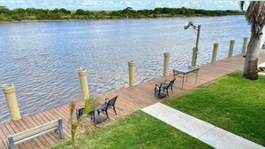 A riverside deck with a table and chairs, a lamp, and a bench. - Waterfront Bunkroom sits on the Colorado river. (Matagorda)