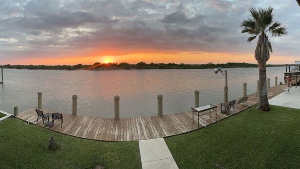 A waterfront property with a dock, a palm tree, and a sunset view. - Waterfront Bunkroom sits on the Colorado river. (Matagorda)