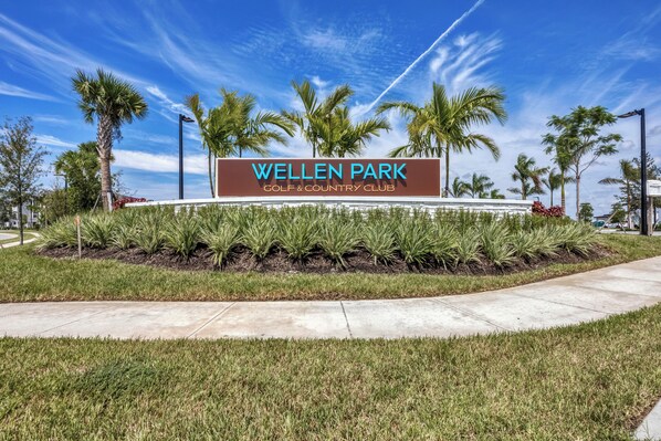 Placa de Wellen Park Golf & Country Club cercada por palmeiras e grama bem cuidada.