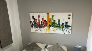 Een keurig opgemaakt bed met een zwaan-kussen, een stadsgezichtschilderij aan de muur en een bedlampje.
