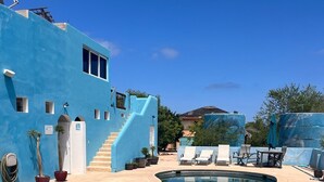 A swimming pool with a blue-tiled edge, surrounded by lounge chairs and a staircase leading to a building with a blue facade. - Cabo Pulmo Beach Resort (Cabo Pulmo)