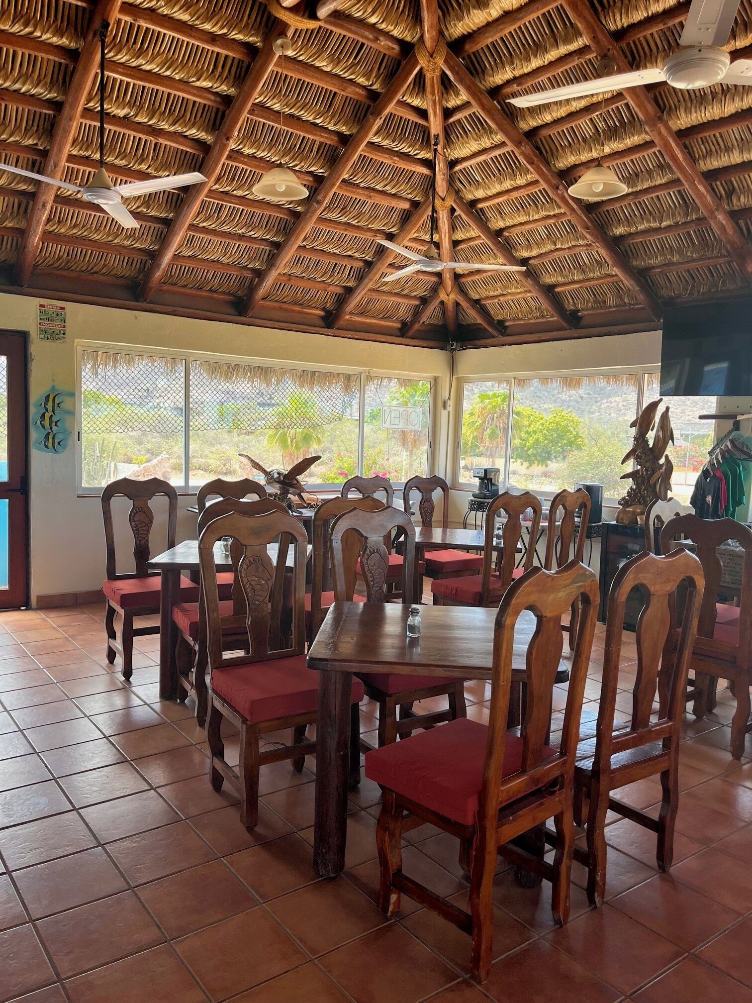 A restaurant with wooden tables and chairs, a thatched roof, and large windows.