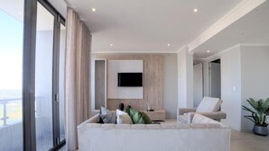 Un soggiorno moderno con un divano ampio, una TV a schermo piatto montata sulla parete e una porta vetrata scorrevole che dà su uno spazio esterno.