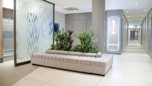Una hall moderna con zona salotto, un pannello in vetro con motivi geometrici e un corridoio con porte numerate.