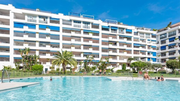 A hotel with a swimming pool, multiple balconies, and palm trees. - Apartment in Terrazas de Banús for 4 people | 13-4-1 (Puerto Banús - Marbella)