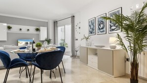 A modern dining area with a round table, blue chairs, and a minimalist kitchen in the background. - Apartment in Terrazas de Banús for 4 people | 13-4-1 (Puerto Banús - Marbella)