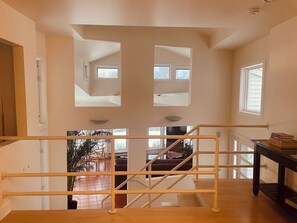 A high-ceilinged room with a staircase, a view of the outdoors, and a window with blinds.