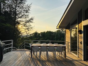 A wooden deck with a table and chairs, a railing, and a view of trees and a building.