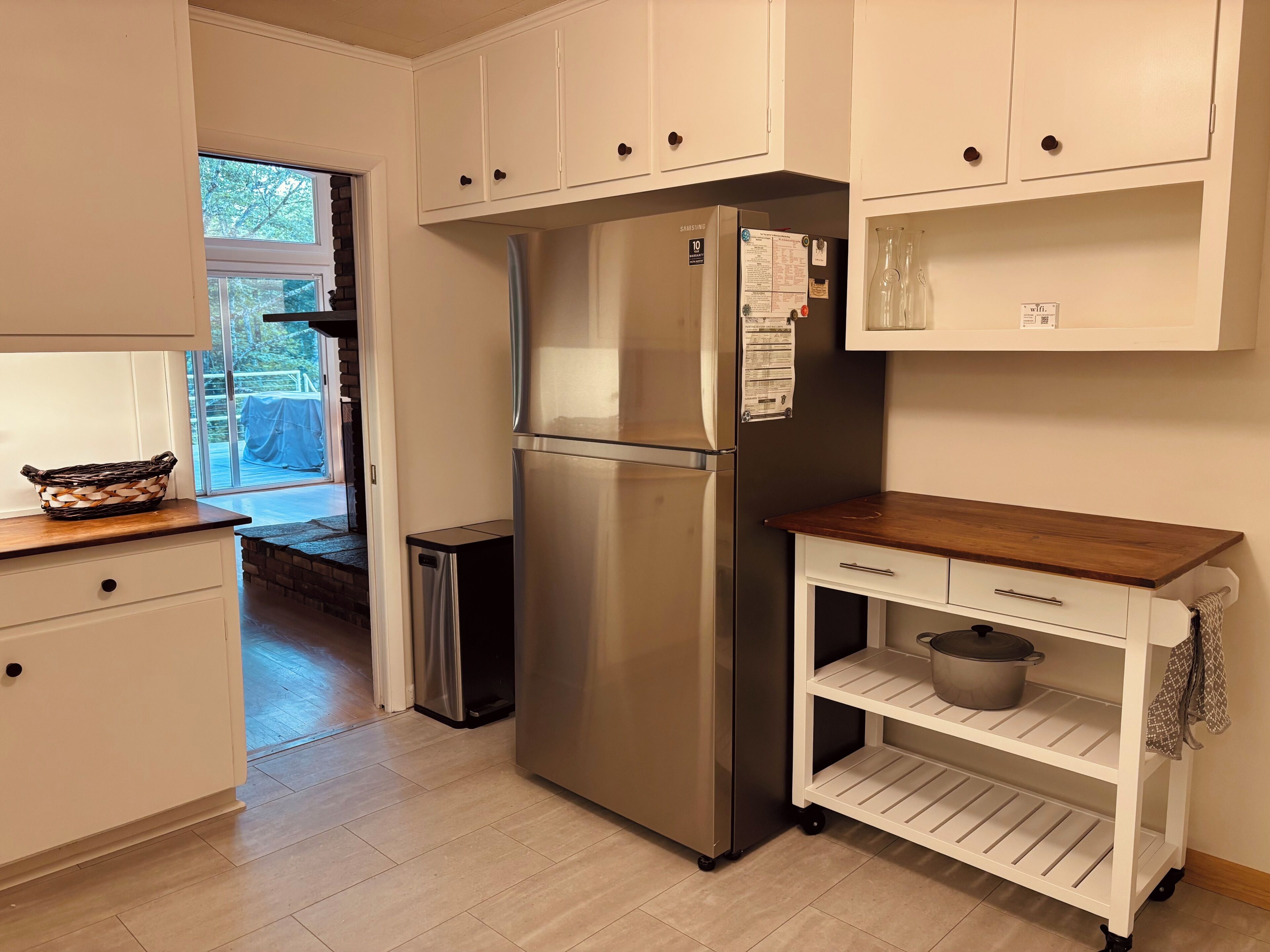 A kitchen with white cabinets, a stainless steel refrigerator, a small trash bin, and a wooden countertop.