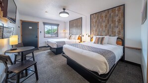 Habitació d'hotel amb dos llits, un escriptori, una cadira, una làmpada i un ventilador de sostre.