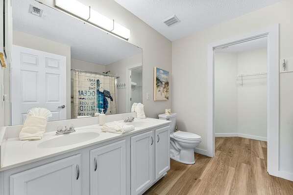 A bathroom with a white vanity, a large mirror, a toilet, and a shower area. - Coastal Charm, Private Pool, Private Beach Access! (Destin)