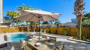 A backyard with a swimming pool, a dining table set with plates and cutlery, and a large umbrella. - Coastal Charm, Private Pool, Private Beach Access! (Destin)