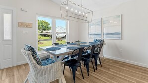 A dining area with a glass table, black chairs, and a hanging light fixture. - Coastal Charm, Private Pool, Private Beach Access! (Destin)