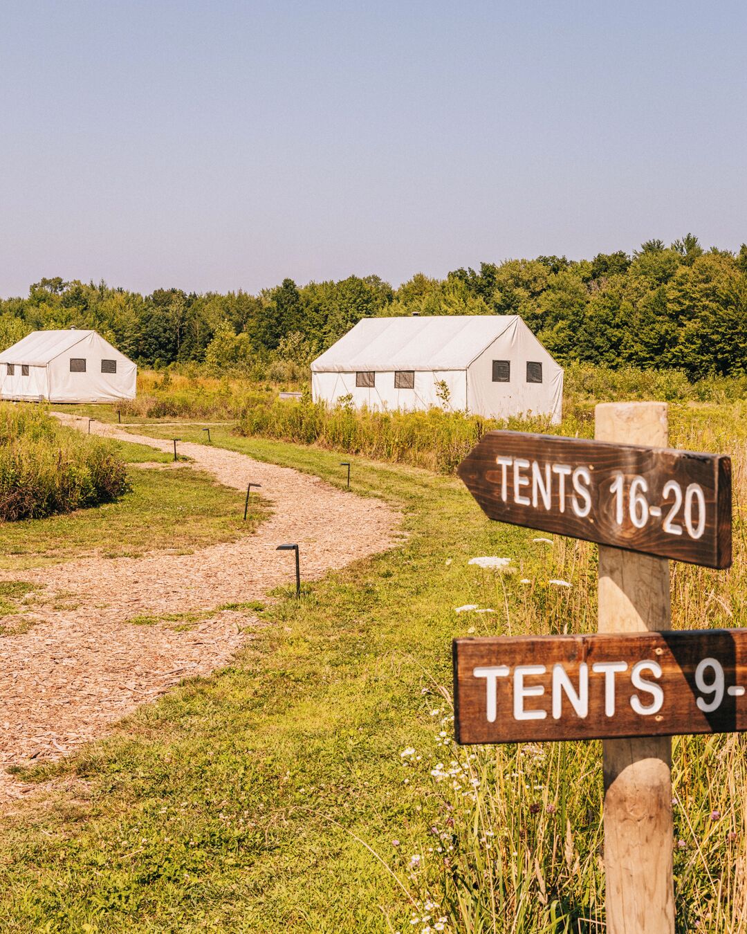 A rural setting with two white tents labeled "TENTS 16-20" and "TENTS 9-10" on a wooden signpost.